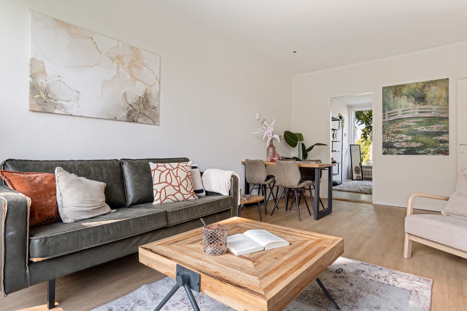 Sfeervolle zithoek met verkoopstyling, met een comfortabele bank, kunst aan de muur en een doorkijk naar de eethoek
