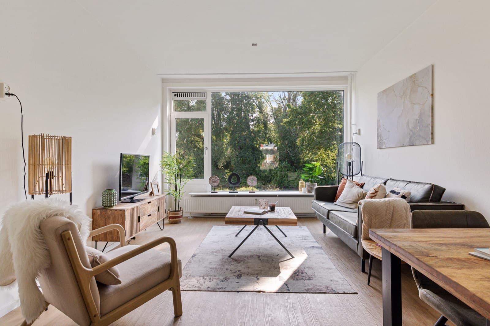 Ruime woonkamer die Buurma Vastgoedservice heeft gestyled voor de verkoop, met een lichte bank en een groot raam met uitzicht op groen